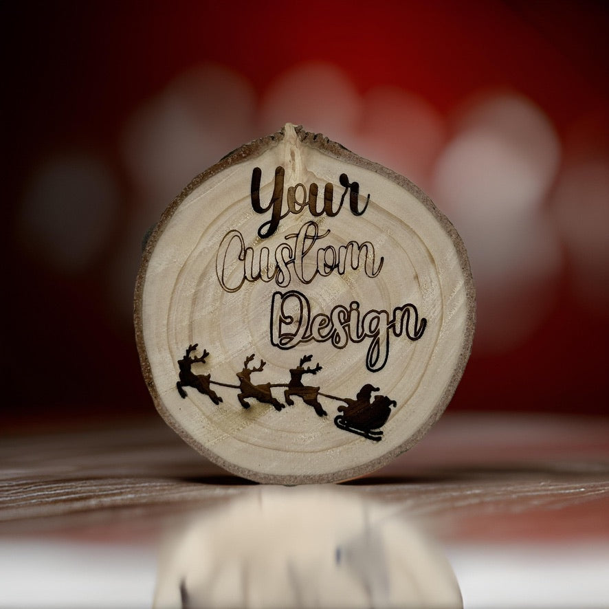 A round natural wood slice ornament with a hanging loop, featuring the text 'Your Custom Design' and a black silhouette of Santa Claus with reindeer. The ornament is set against a warm, blurred red background.