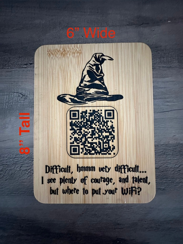 A rectangular wooden plaque with rounded corners, shown on a dark wood surface. The plaque has a black printed illustration of a witch's hat, a QR code, and the text 'Difficult, hmm mmm very difficult.