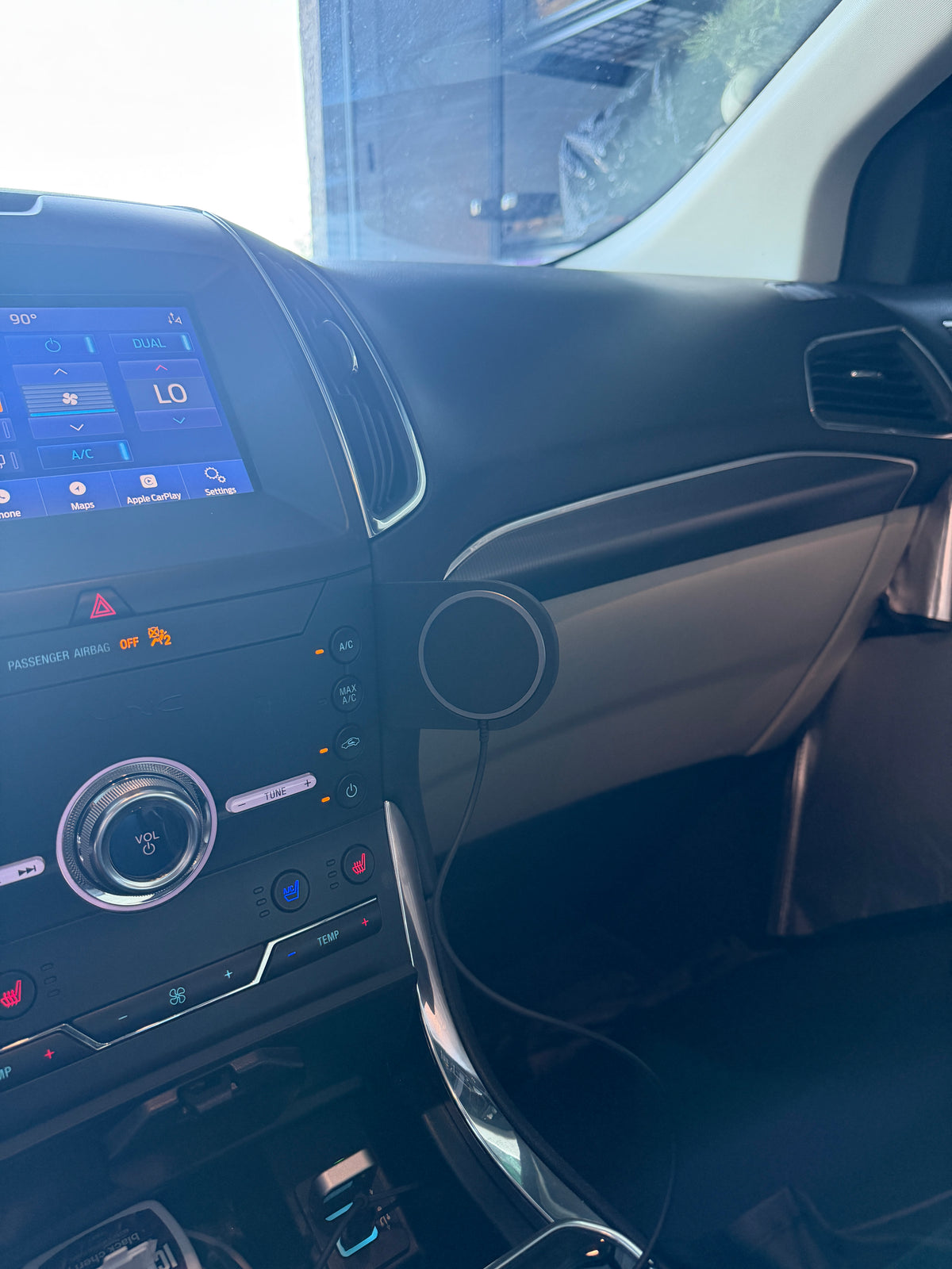A close-up view of a car's interior dashboard and center console, showing a touchscreen display, climate controls, and a circular speaker mounted on the door panel.