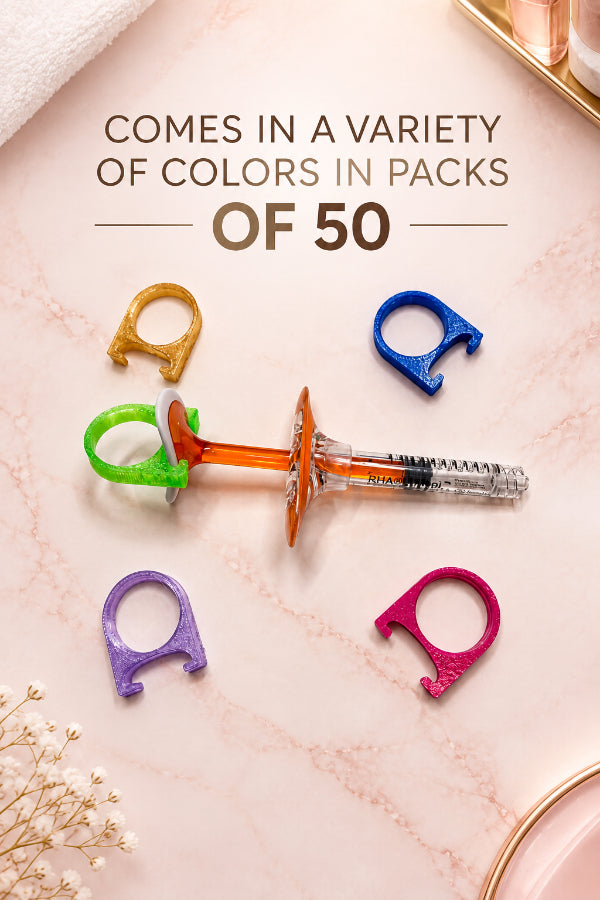 An orange and clear plastic IV drip chamber with a syringe attached, arranged on a white surface alongside five small colorful ring-shaped accessories in gold, green, blue, purple, and pink.