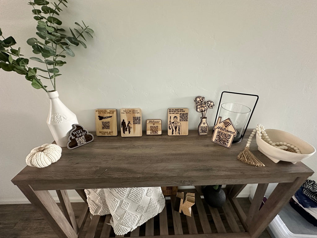 A rustic dark wood console table styled with home decor items including a white vase with greenery, small wooden picture frames, a glass candle holder, a bowl of white beads, and a white knit throw blanket draped over the lower shelf.
