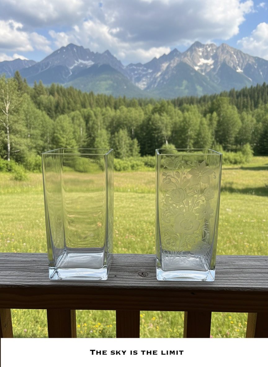 Two clear glass vases on a wooden table with a scenic background of mountains and trees.