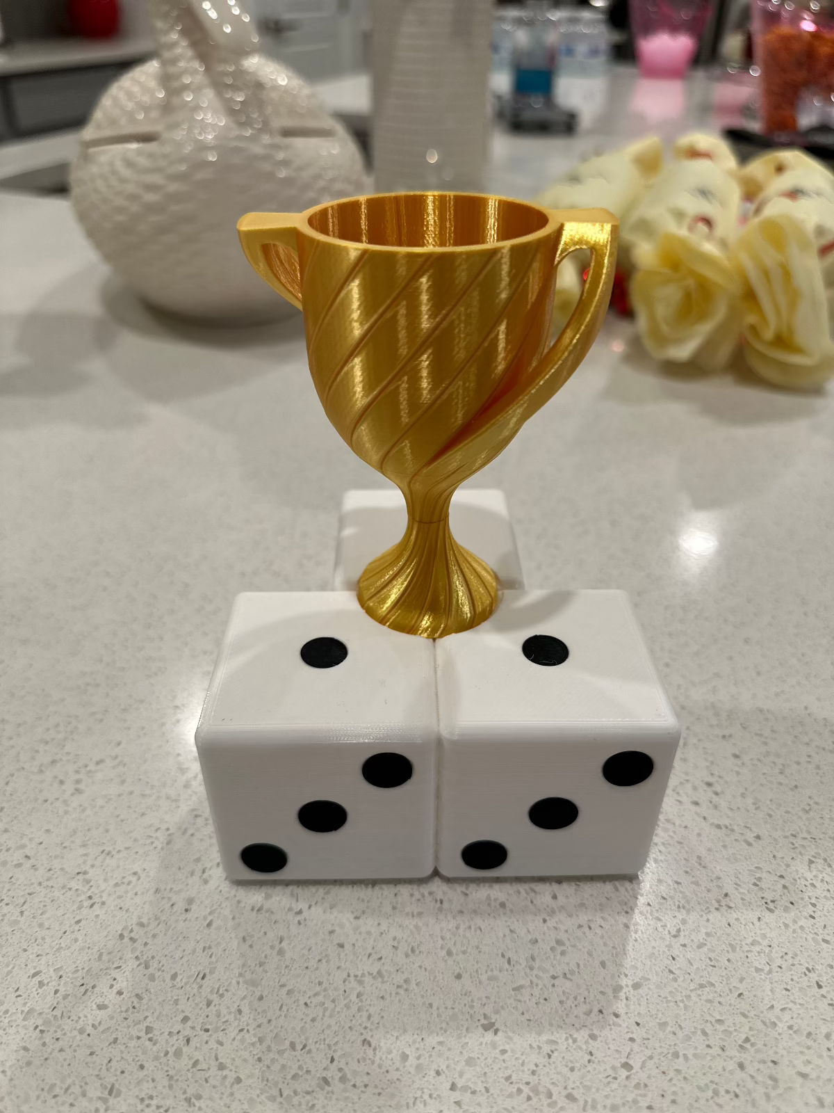 Gold trophy cup on a base of three white dice on a kitchen counter