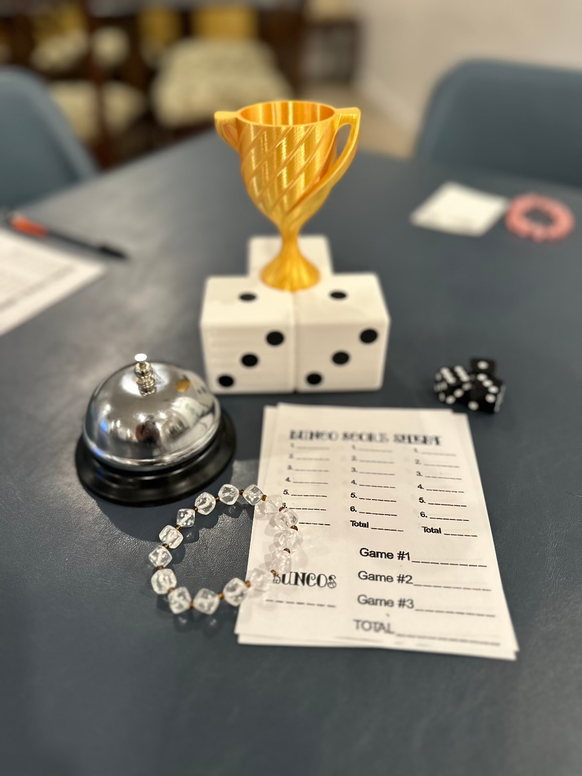 Gold Bunco trophy on a dice base on a game table with a bell, dice and a score sheet