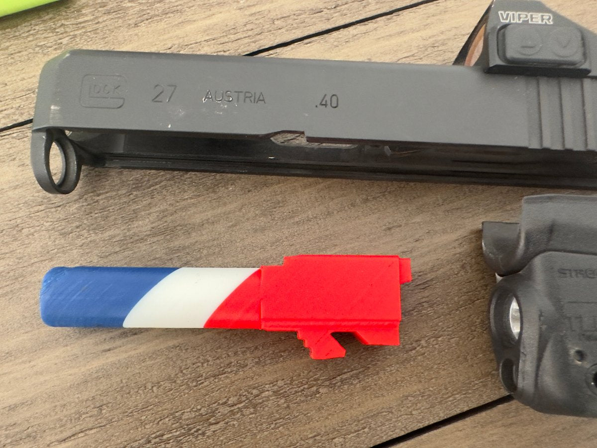 Red, white and blue training safety barrel next to a Glock 27 slide and frame on a wood table