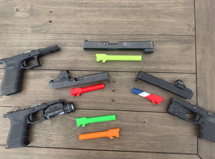 Disassembled Glock frames and slides on a wood table with plastic training safety barrels in green, red, red-white-and-blue, light green and orange