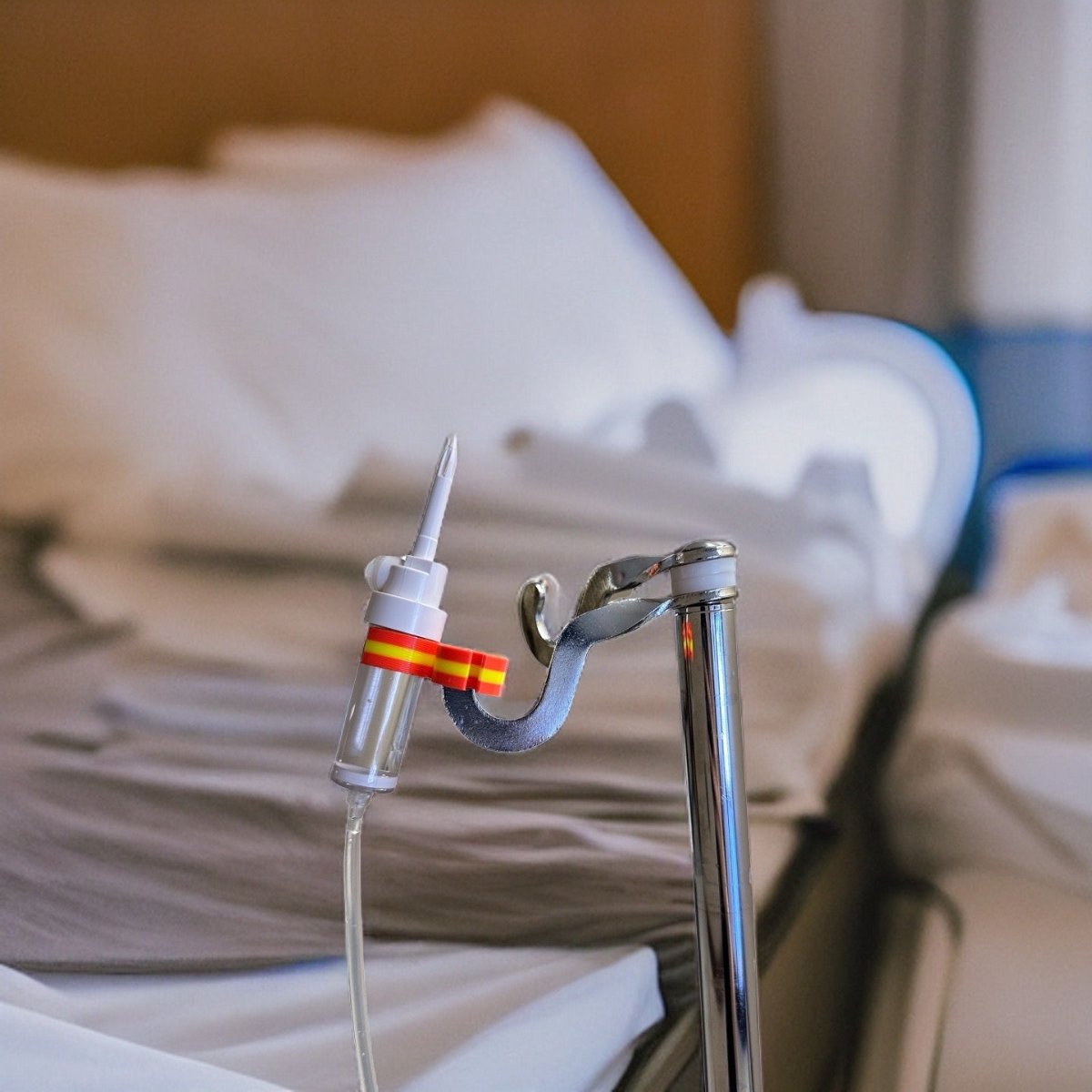 Orange drip chamber holder holding an IV drip chamber on an IV pole beside a hospital bed