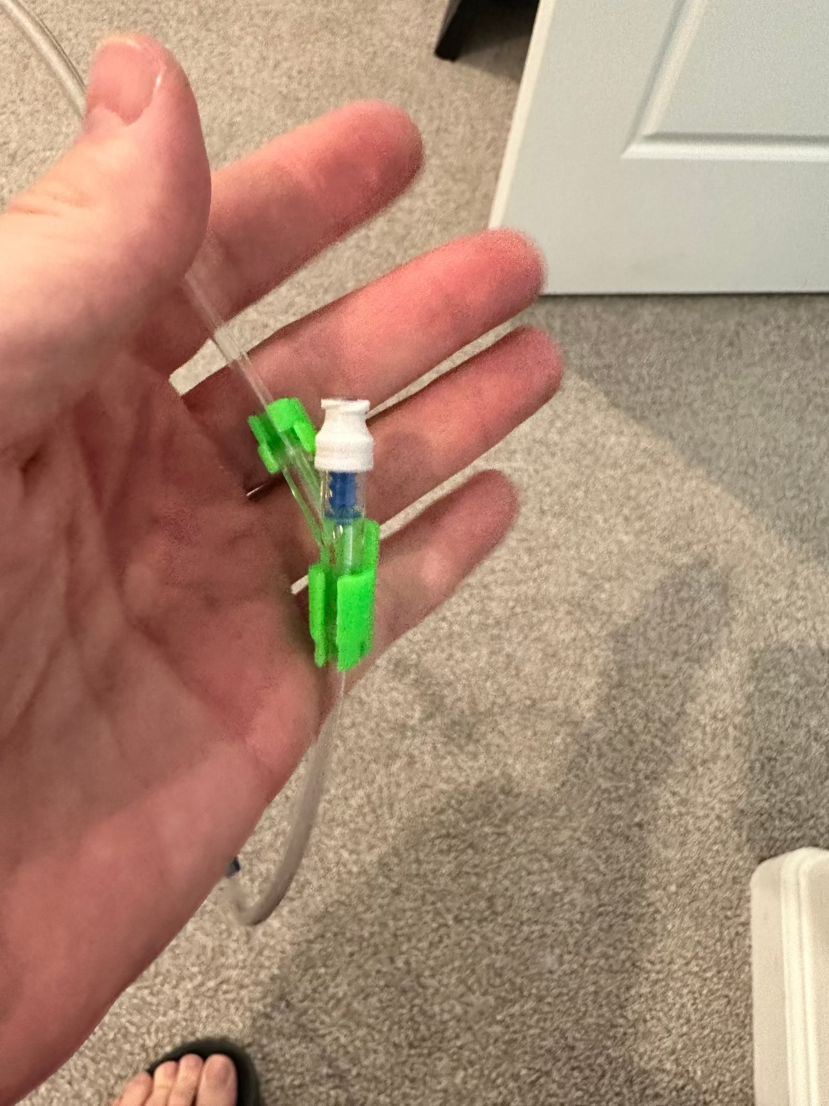 Hand holding IV tubing with a green port identifier on the medication port