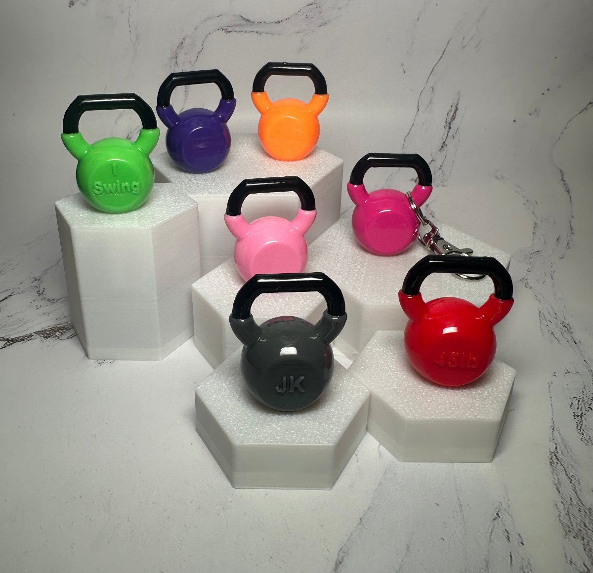 Mini kettlebell keychains in green, purple, orange, pink, red and black on white display stands