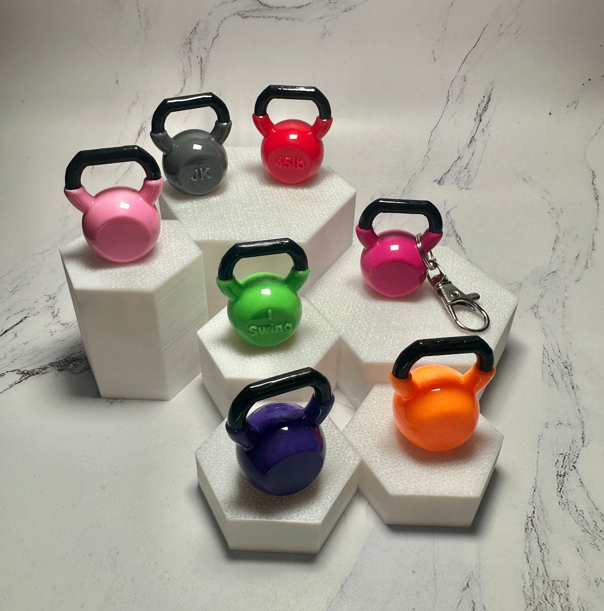 Mini kettlebell keychains in several colors arranged on stacked white display stands