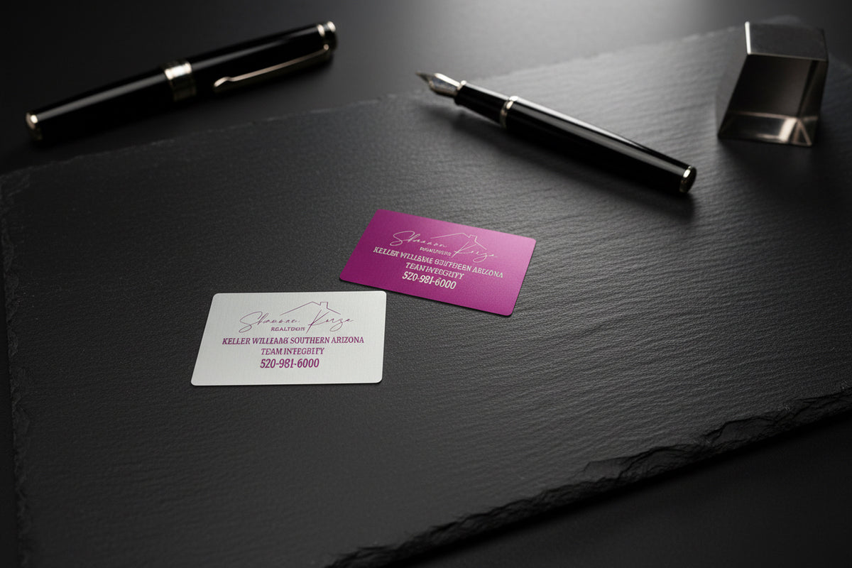 Pink engraved metal business card on a dark desk with pens