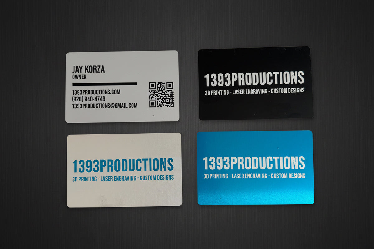 Four laser-engraved metal business cards in silver, black and blue with 1393Productions branding on a dark surface