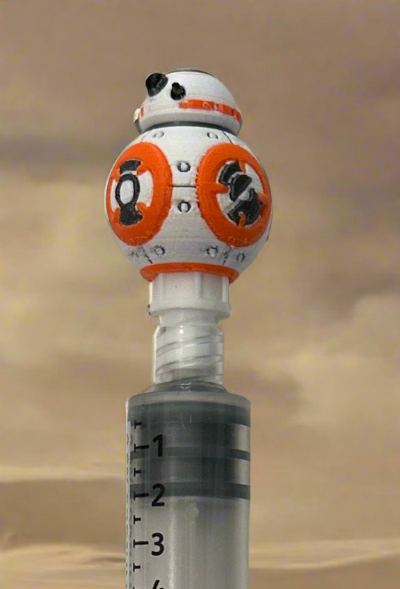 Orange and white rolling droid flush cap holder on top of a 10 mL saline flush syringe in a desert setting