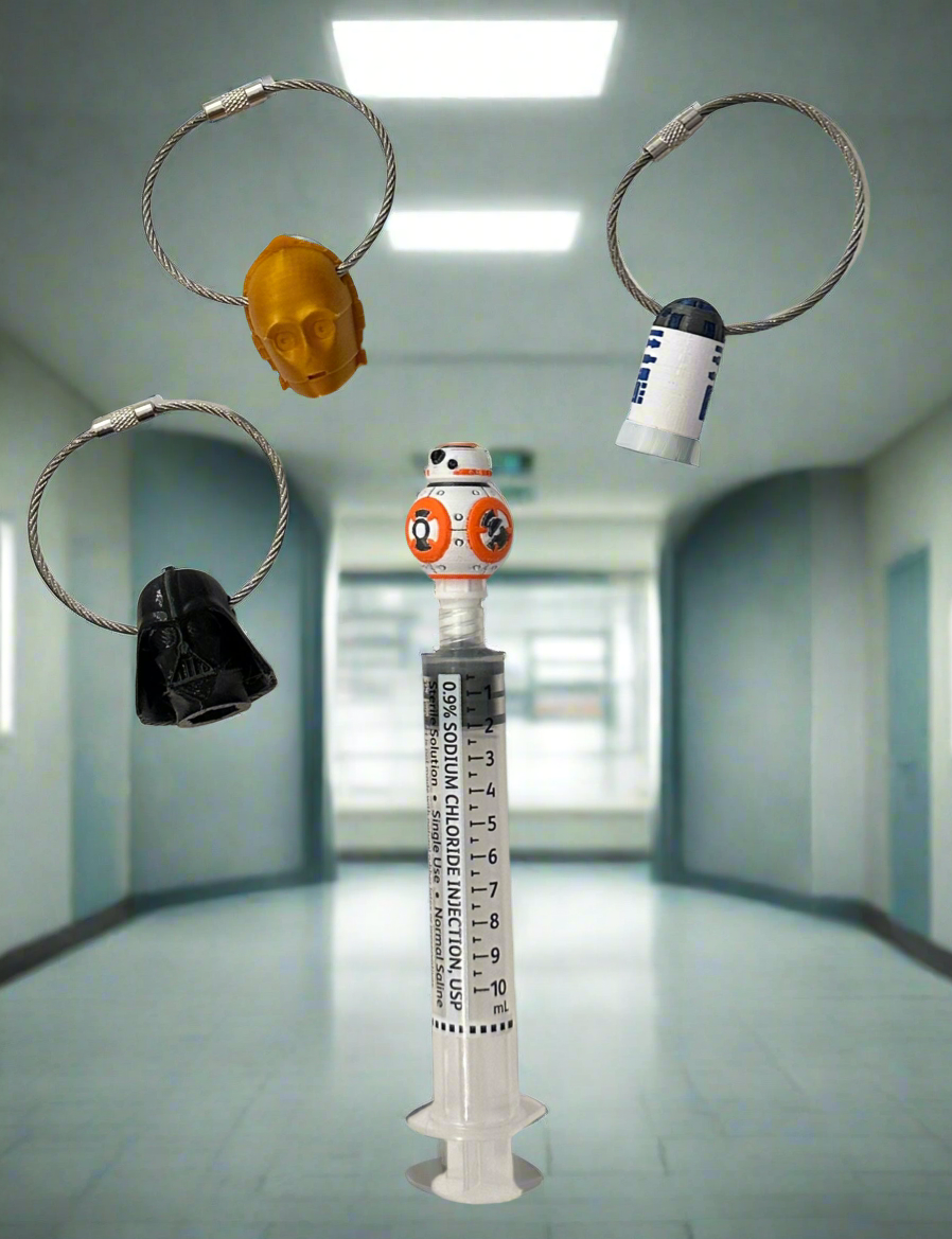 All four sci-fi character flush cap holders hanging on rings around a saline flush syringe in a hospital hallway