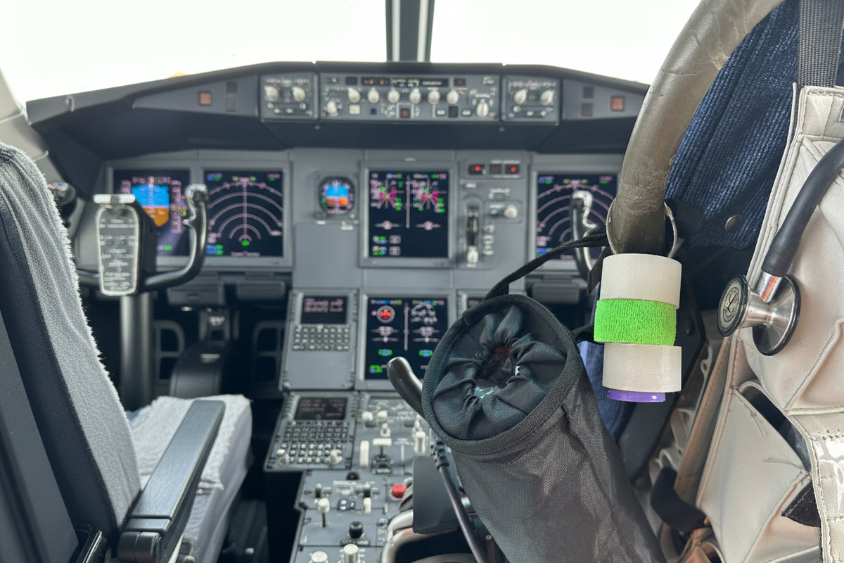 Tape holder with a roll of green tape hanging by a steel cable clasp in an aircraft cockpit