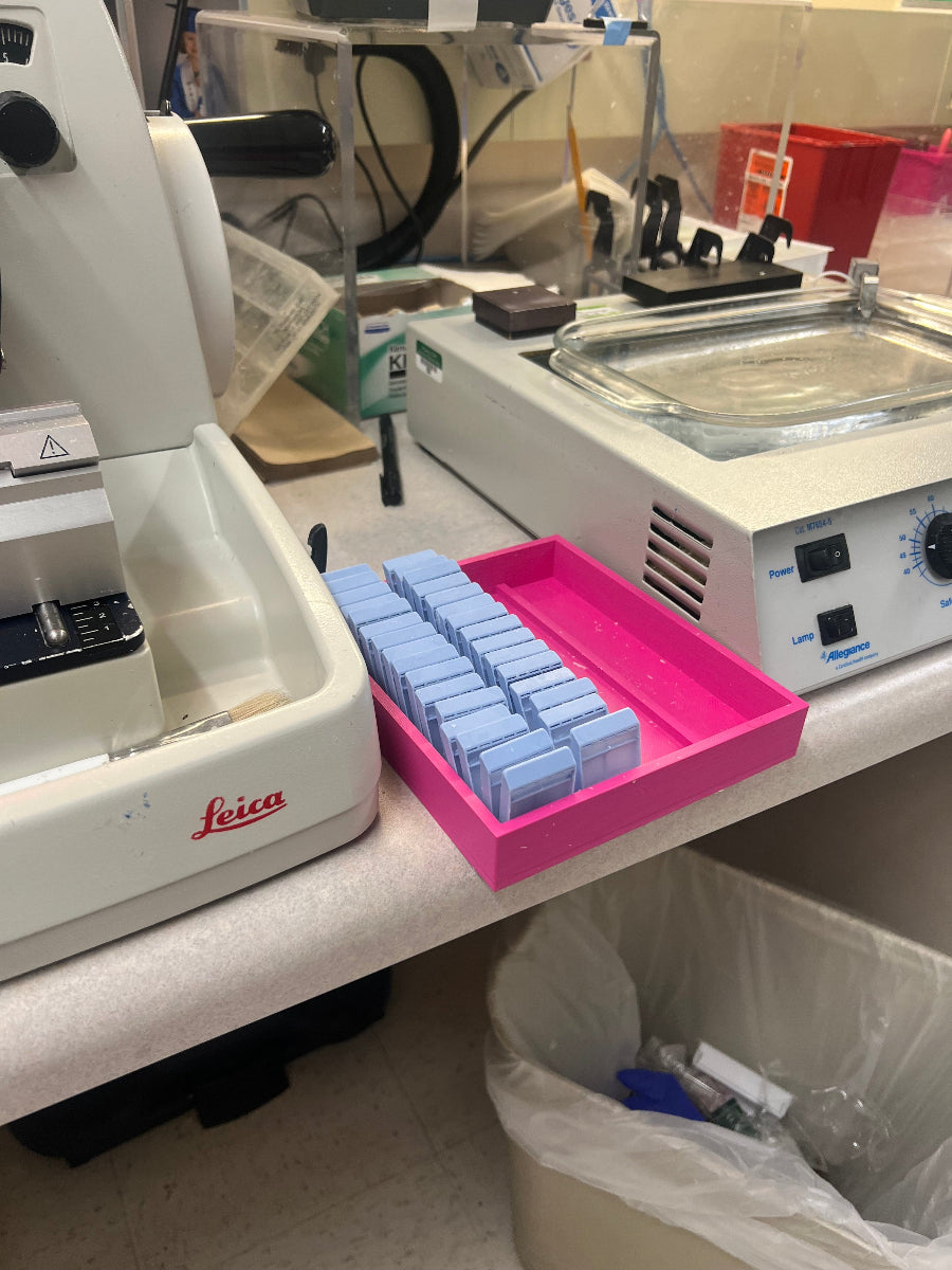 Pink tissue cassette rack holding blue cassettes on a lab bench beside histology equipment