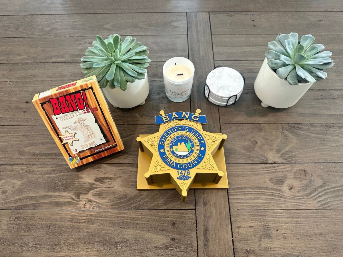 Gold sheriff star card box for the card game BANG! on a table with game cards and plants