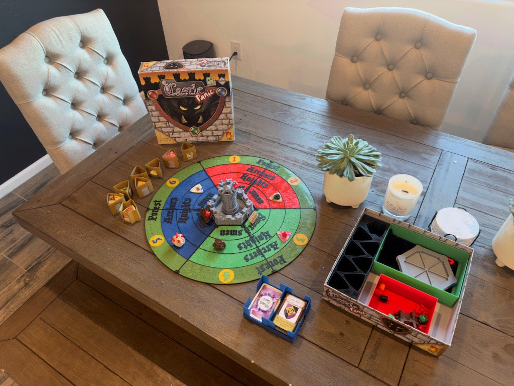 Round six-piece Castle Panic replacement board on a dining table with the game box and organizer