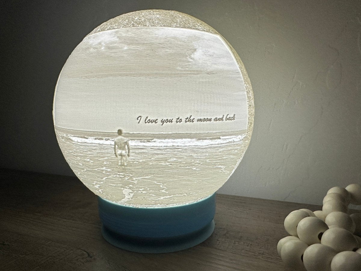 Lit 3D printed moon lamp on a blue base on a dark table
