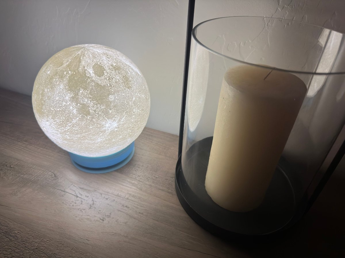Glowing moon lamp next to a candle in a glass holder