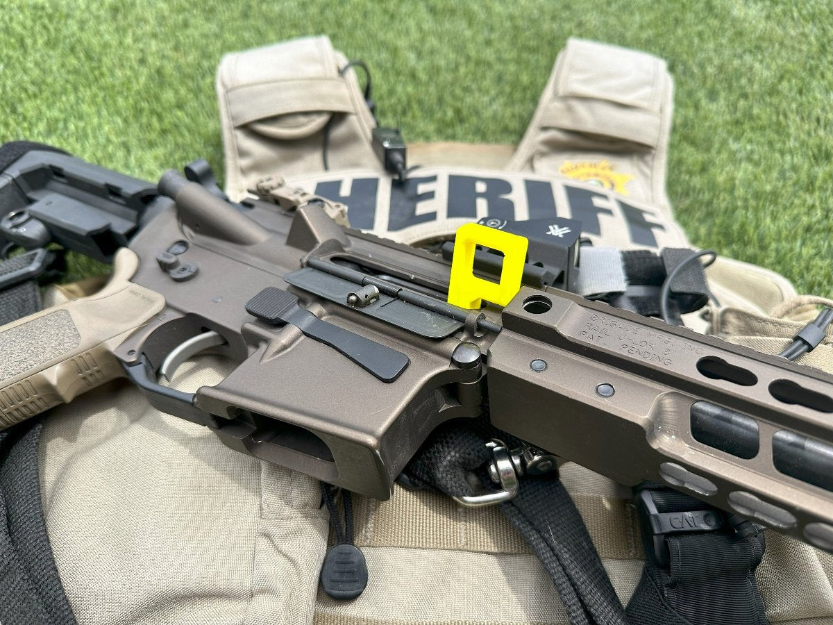 Yellow chamber safety flag inserted in an AR-15 rifle on a sheriff's vest on grass