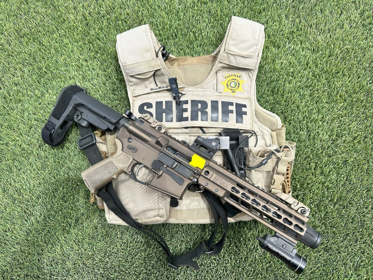 AR-15 rifle with a yellow chamber safety flag lying on a sheriff's vest on grass